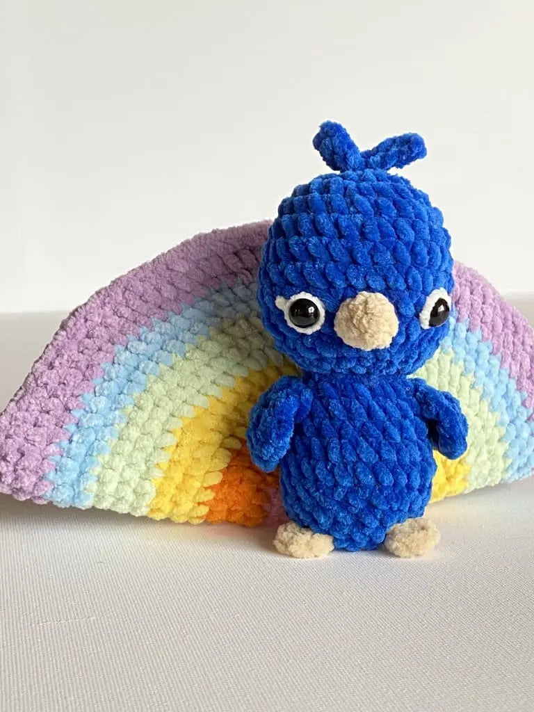 A blue crochet peacock with a rainbow tail from tchip tchip a crochet pattern shop